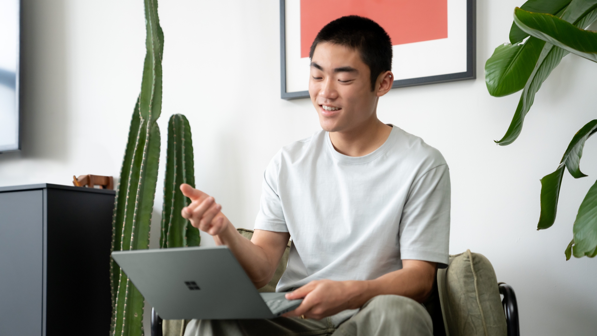 Junger Mann, der in einem modernen Zimmer mit Zimmerpflanzen fröhlich einen Laptop benutzt.