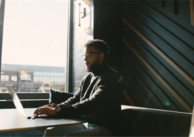 A person with specs sitting at a table with a computer
