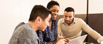 A woman and a couple of men smiling, working together and pointing at a laptop