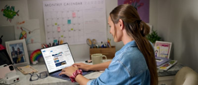 A person sitting at a desk using a laptop with a calendar featuring sticky notes in the background.