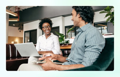 Two people sitting in a modern office lounge with laptops and notebooks.