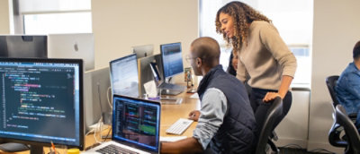 A man and woman looking at computers on a desk.