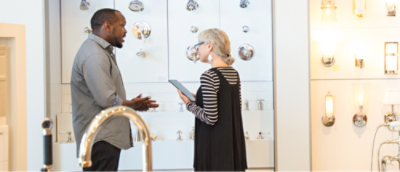Two people stand in a brightly lit showroom discussing plumbing fixtures.