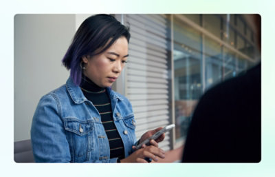 Person holding a smartphone while wearing a denim jacket in an indoor setting.