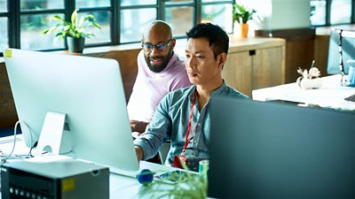 A person sitting at a desk using a computer with a coworker sitting beside