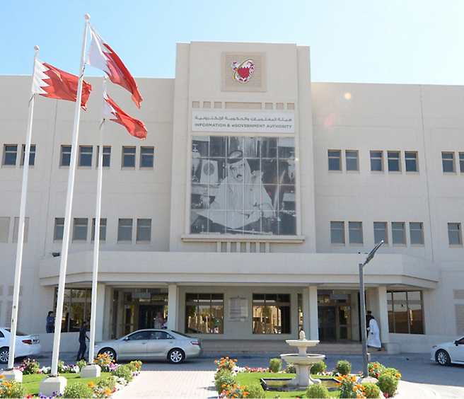 Facade of the information & government authority building in bahrain with flags and a large photograph of a dignitary.