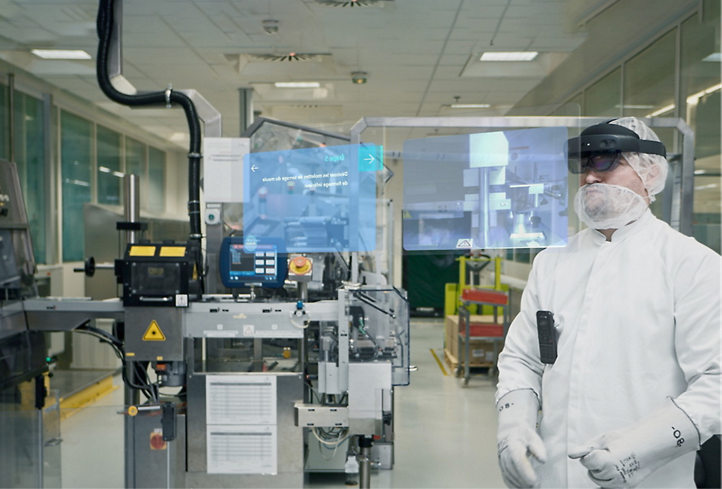 A technician in a cleanroom suit and augmented reality glasses analyzing data in front of industrial machinery.