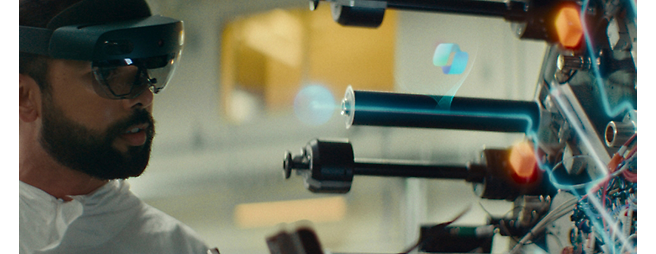 Un hombre con gafas de realidad aumentada trabaja en un brazo robótico complejo con elementos digitales flotantes a su alrededor.