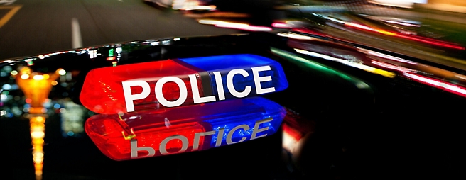 Illuminated police car roof lights with red, blue, and white colors on a blurred city street background at night.