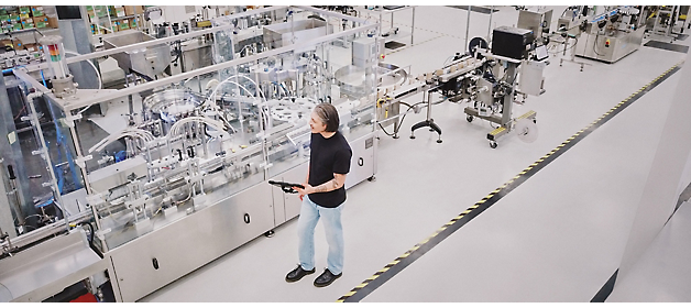 A person stands observing an automated production line in a clean and modern manufacturing facility.