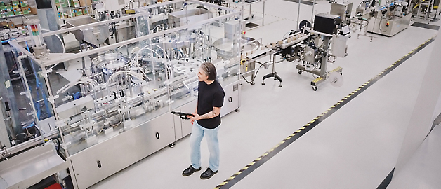 一个人站在干净整洁的现代化生产设施中观察自动化生产线。
