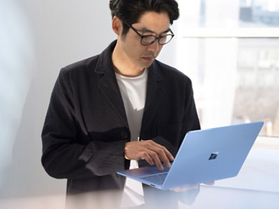 A person wearing glasses is typing on a laptop.