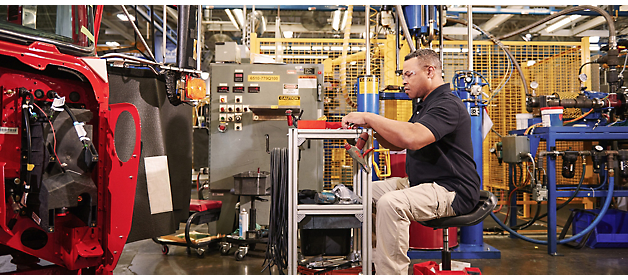 Um trabalhador inspeciona um componente em uma estação de manufatura industrial.