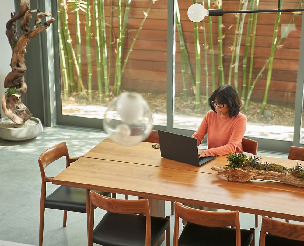 صورة لشخص يجلس على طاولة ويستخدم جهاز كمبيوتر محمول