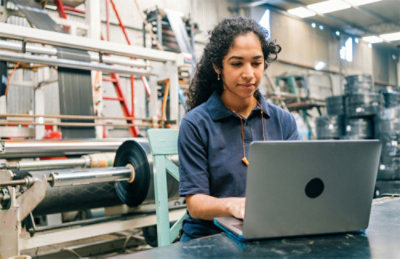 A woman sitting in a factory using a laptop.