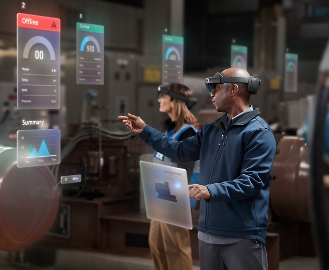 Two individuals using augmented reality headsets to interact with virtual data displays in an industrial environment.