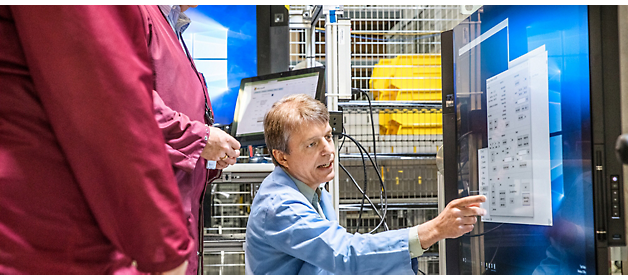 Duas pessoas em uma sala de controle analisando dados em telas de computador.