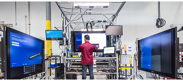 Un tehnician lucrând la echipamente într-un mediu de laborator de înaltă tehnologie înconjurat de monitoare mari.