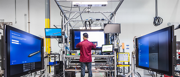 A technician working on equipment in a high-tech laboratory setting surrounded by large monitors.