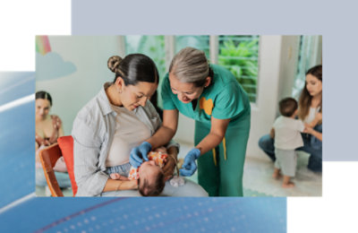 A woman holding a baby while wearing scrubs and gloves.