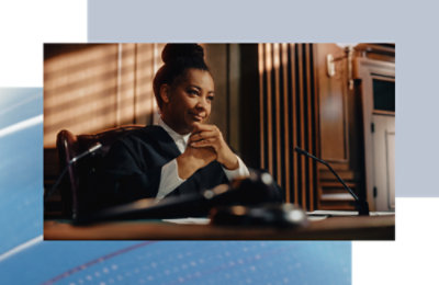 Person seated at a courtroom bench with hands clasped, microphone and wood paneling visible.