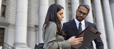 A man in a suit holding a clipboard and a woman in a grey jacket looking at it.