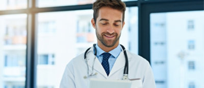 A doctor in a white coat with a stethoscope around his neck looks down and smiles.