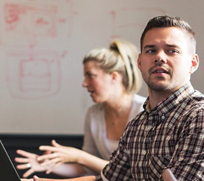 A man and woman sitting at a table looking at a laptop.