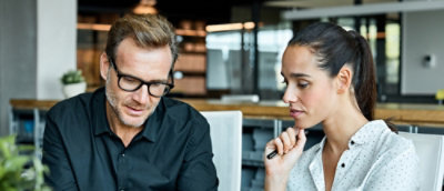 Un hombre con gafas y una mujer con la mano en la barbilla mirándose el uno al otro.