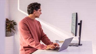 Image 7: A man in a red sweater sitting at a desk typing on a laptop.