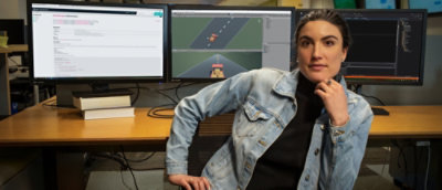 A woman wearing a denim jacket sitting in front of a computer with a video game on the screen.