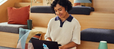 Жінка сидить на дивані й працює за ноутбуком.