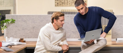 Чоловік сидить на лавці, схрестивши ноги та тримаючи ноутбук.