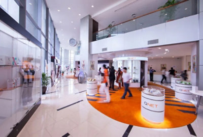 A group of people walking in a building with a white cylinder displaying QNET.