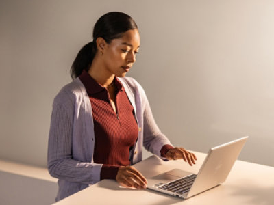 A woman in a sweater typing on a laptop