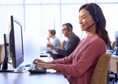 Smiling female call center agent working at computer in a bright office.
