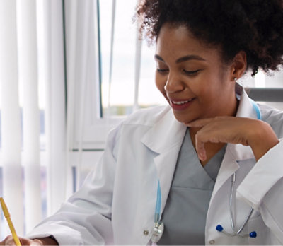 A woman in a white coat, smiling and writing.
