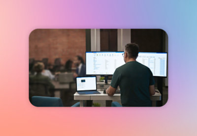 Man working on a computer in a modern office with colleagues in the background.