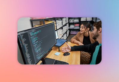 Two people discussing code on a computer screen in an office environment.