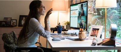 A woman with long hair and glasses sitting at a desk with her hands up.