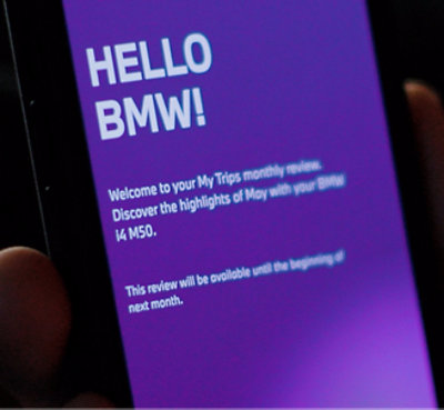 A hand holding a phone displaying a purple screen with text containing a BMW monthly review.