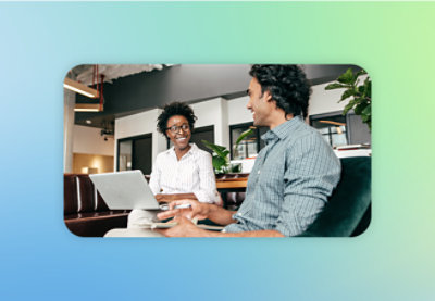Two people sitting on a couch in a modern office setting, one holding a laptop and the other a tablet