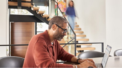 A man with glasses and beard sitting at a desk with a laptop.