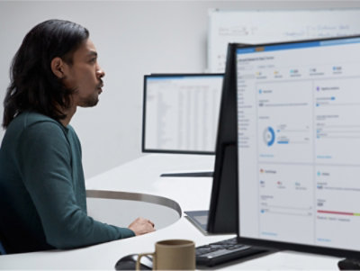 A man with long hair and a beard sitting at a desk looking at a computer screen.