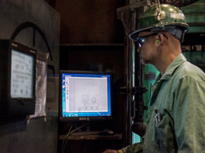 A man wearing a helmet and goggles looking at a computer screen.