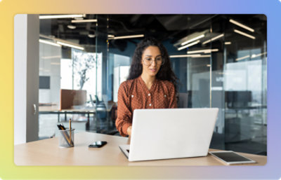 Uma mulher com óculos e cabelo longo encaracolado a trabalhar num portátil num escritório moderno.