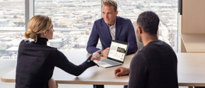 A woman holding a laptop to a man sitting at a table.