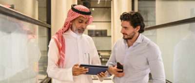 Un bărbat poartă un fular și ținând o tabletă discutând cu un alt bărbat.