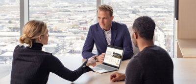 2 bărbați și o femeie stau la o masă cu un laptop.