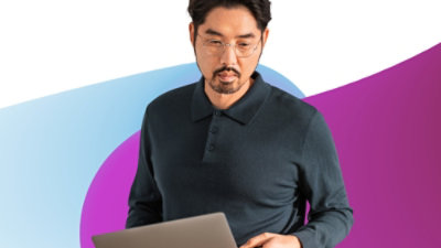 Egy kék inges férfi egy laptopot tart, összpontosítva és a munkájába merülve.